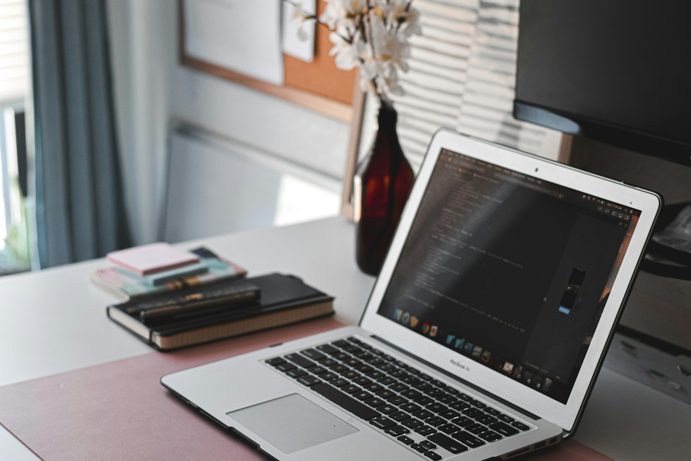A photographed workspace with a laptop, notebooks, and natural window light