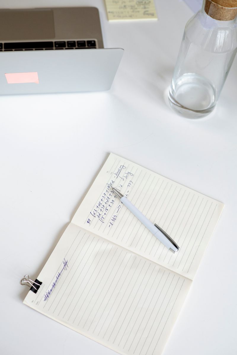 Notes and pen beside laptop on tidy white desk